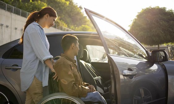 Patient en fauteuil roulant aidé à monter dans un taxi